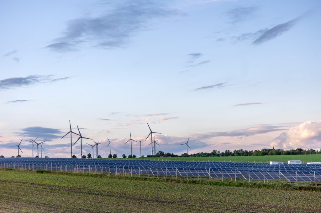 Solar panels in a field with wind turbines on the horizon — renewable energy mix