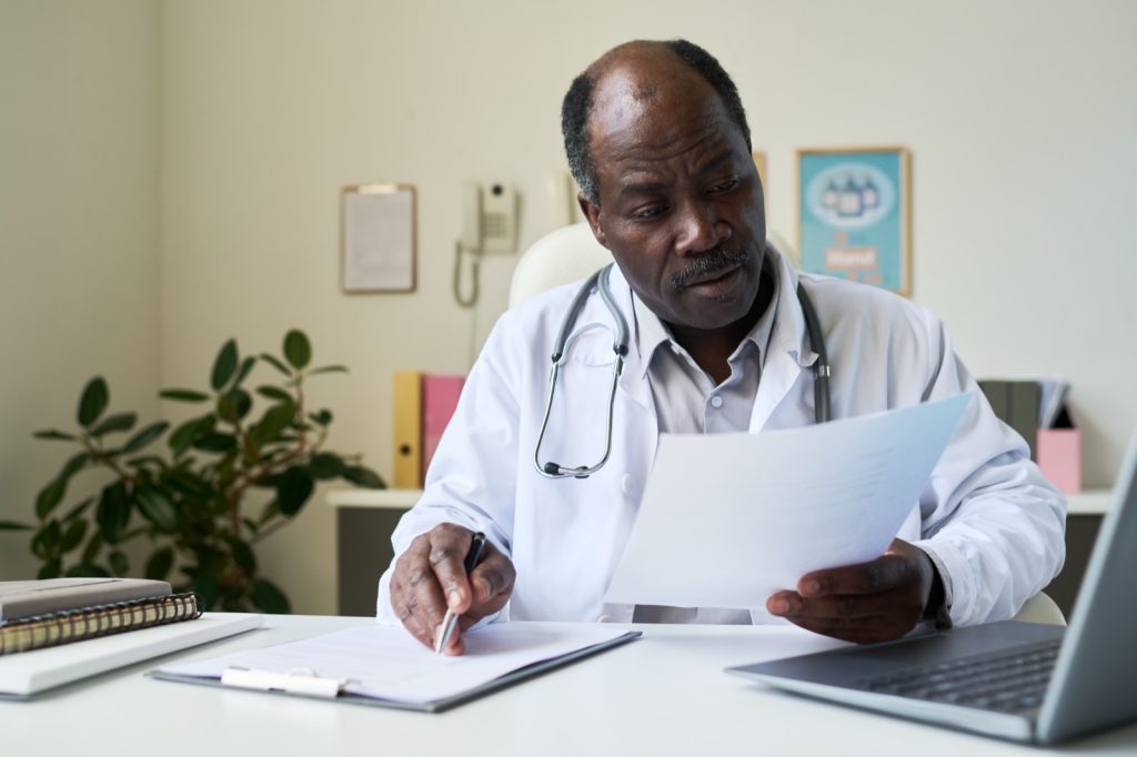 An african doctor carefully reviewing patient documents. Berkley risk conducts a structured review of cover, extensions and retroactive dates for medical malpractice placements