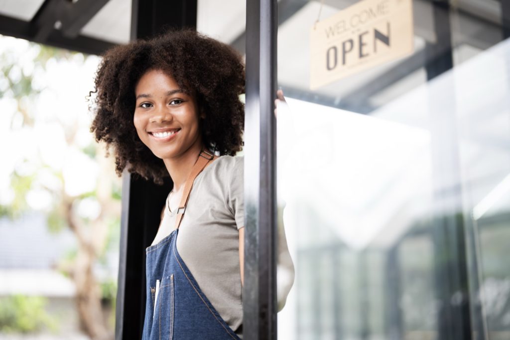 African small business owner standing outside her coffee shop. Retail and hospitality is one of the primary sa industries that arranges public liability insurance