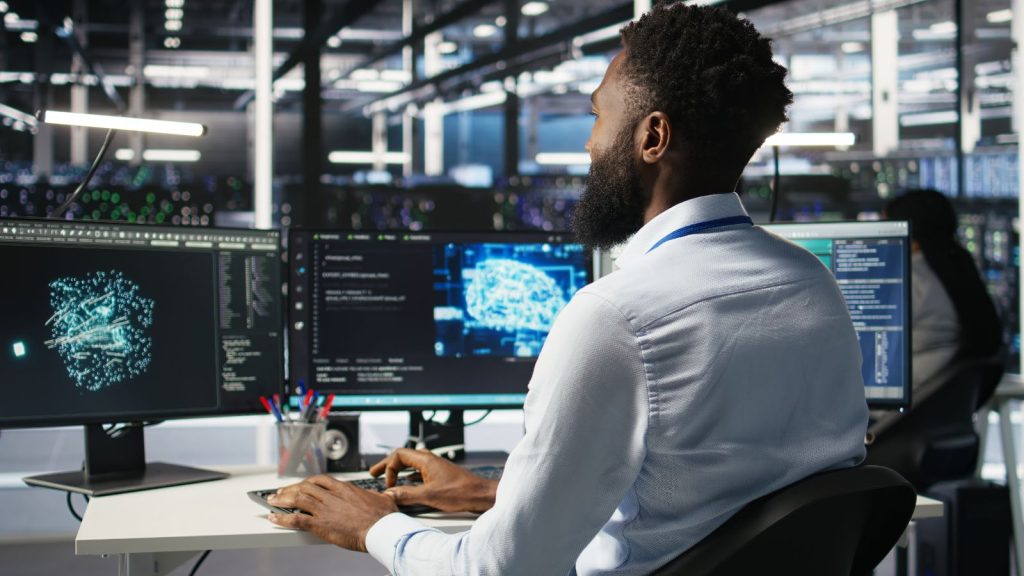 An engineer monitoring an ai model on multiple screens, where testing and oversight shape professional indemnity cover