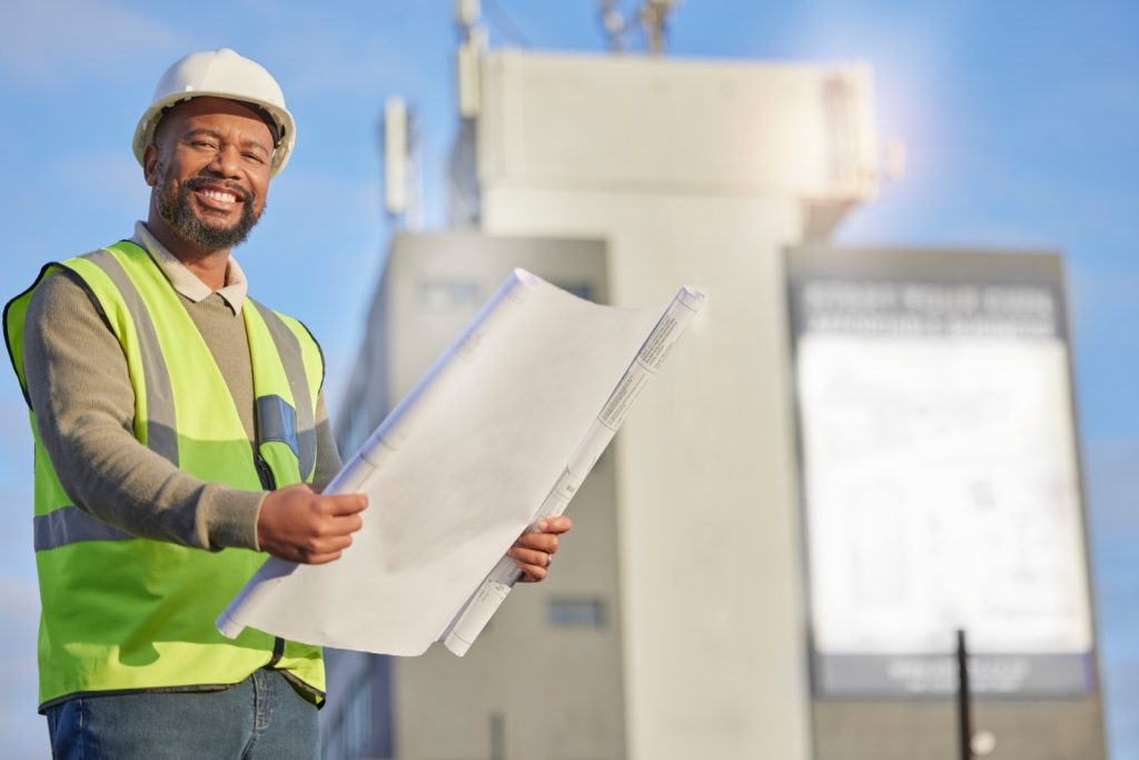 Contractor holding blueprints outside a building under construction, representing design and build responsibility