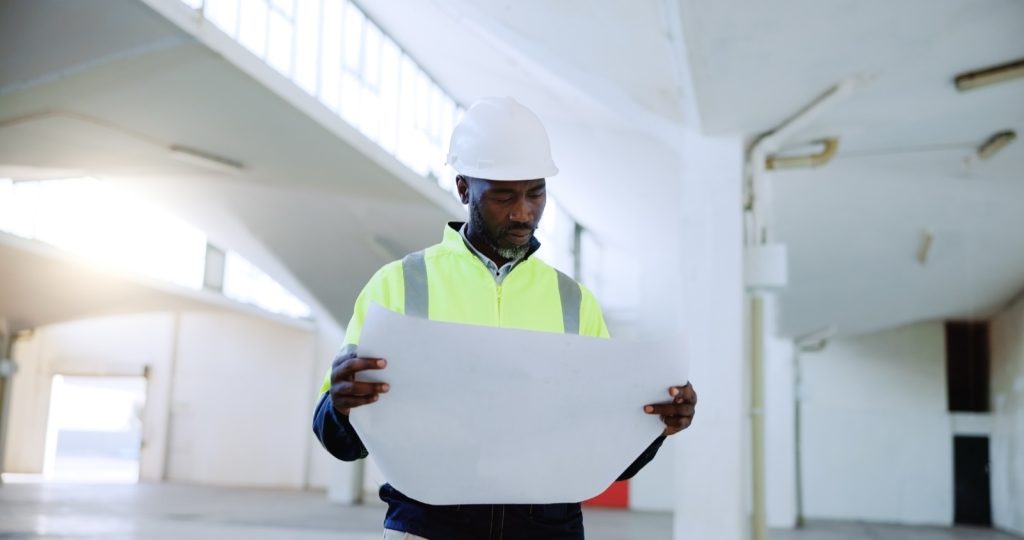 Site professional in a hard hat and high-visibility vest reviewing building plans inside a property under construction