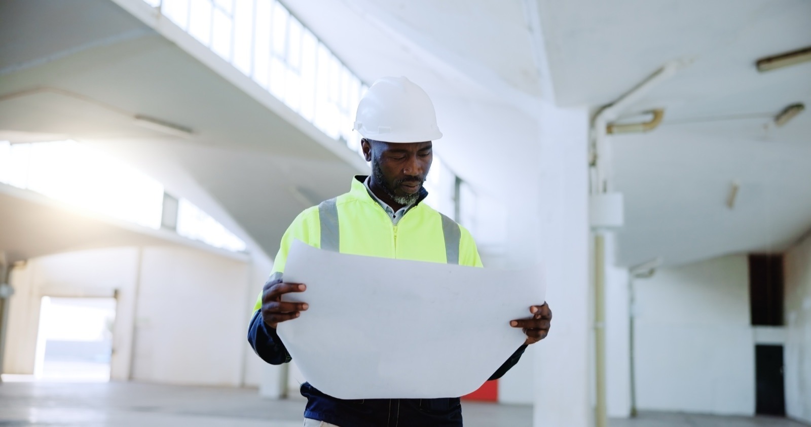 Insurance During Construction: What Property Owners And Developers Need To Know 6 Site professional in a hard hat and high-visibility vest reviewing building plans inside a property under construction