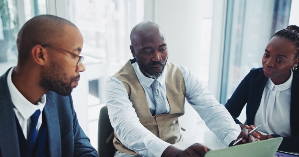 Three african business professionals in a serious discussion reviewing risks around a laptop in a boardroom